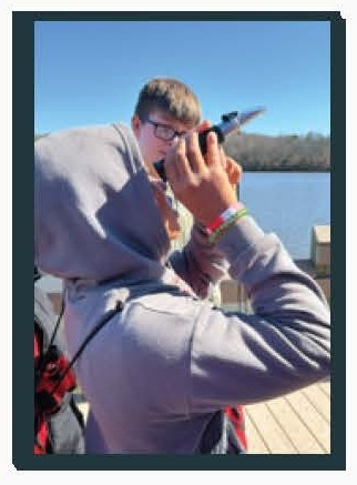 Students by water on pier using a viewing tool